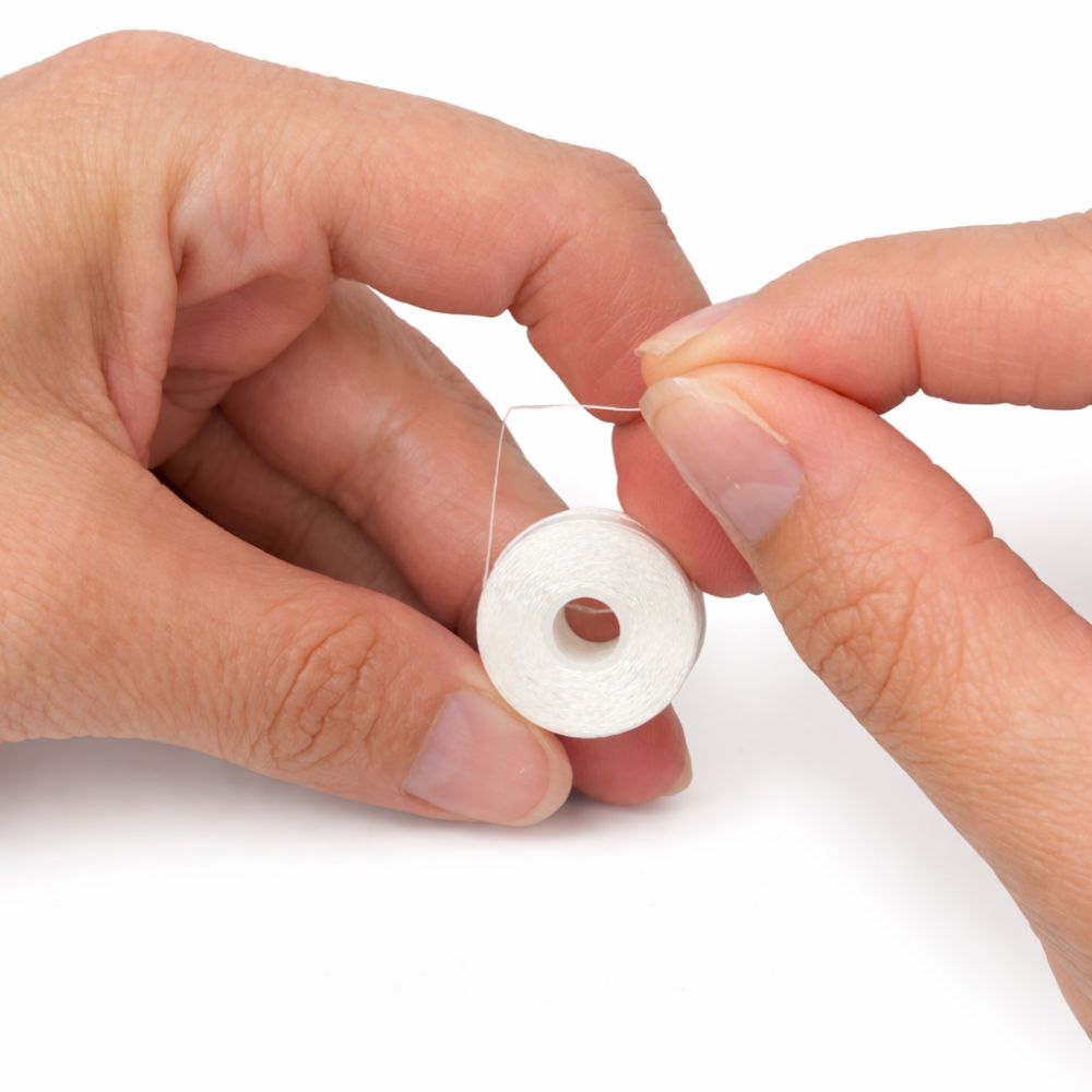 Close-up of hands holding a white embroidery bobbin thread on a white background