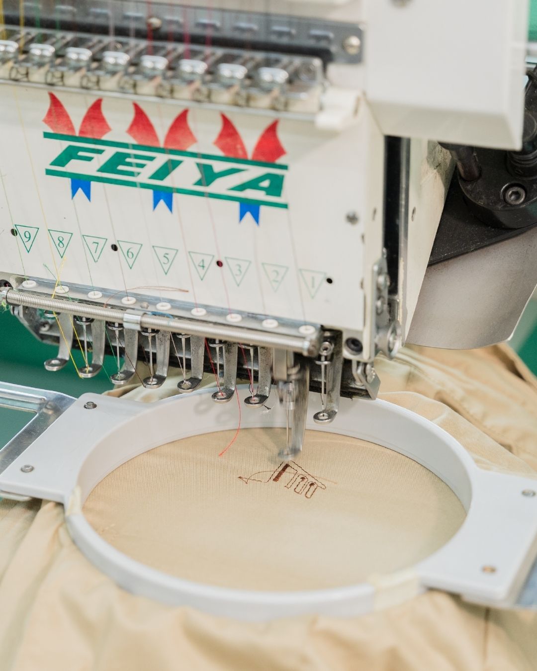Embroidery machine with 'Feiya' branding on a beige fabric background