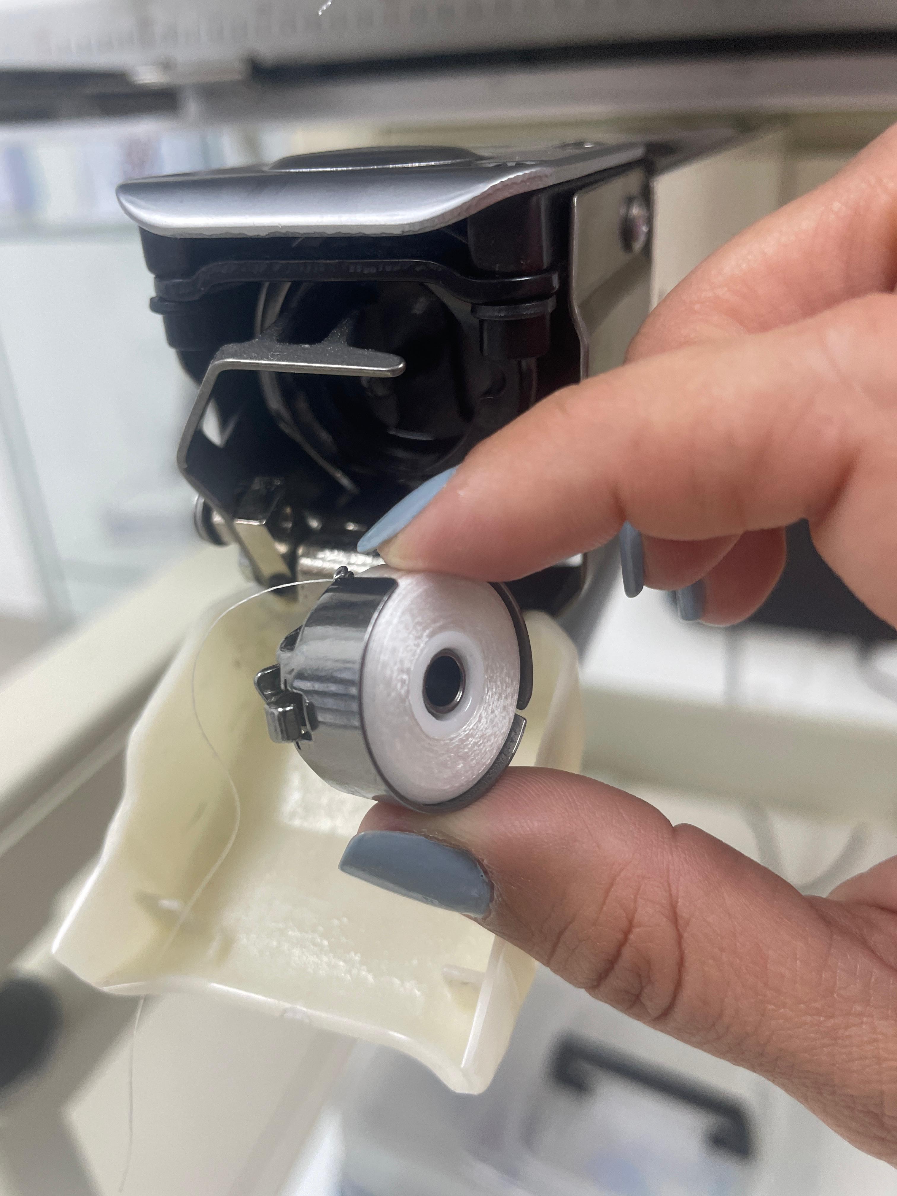 A person holding a small mechanical component  of an embroidery machine  where the bobbin fits