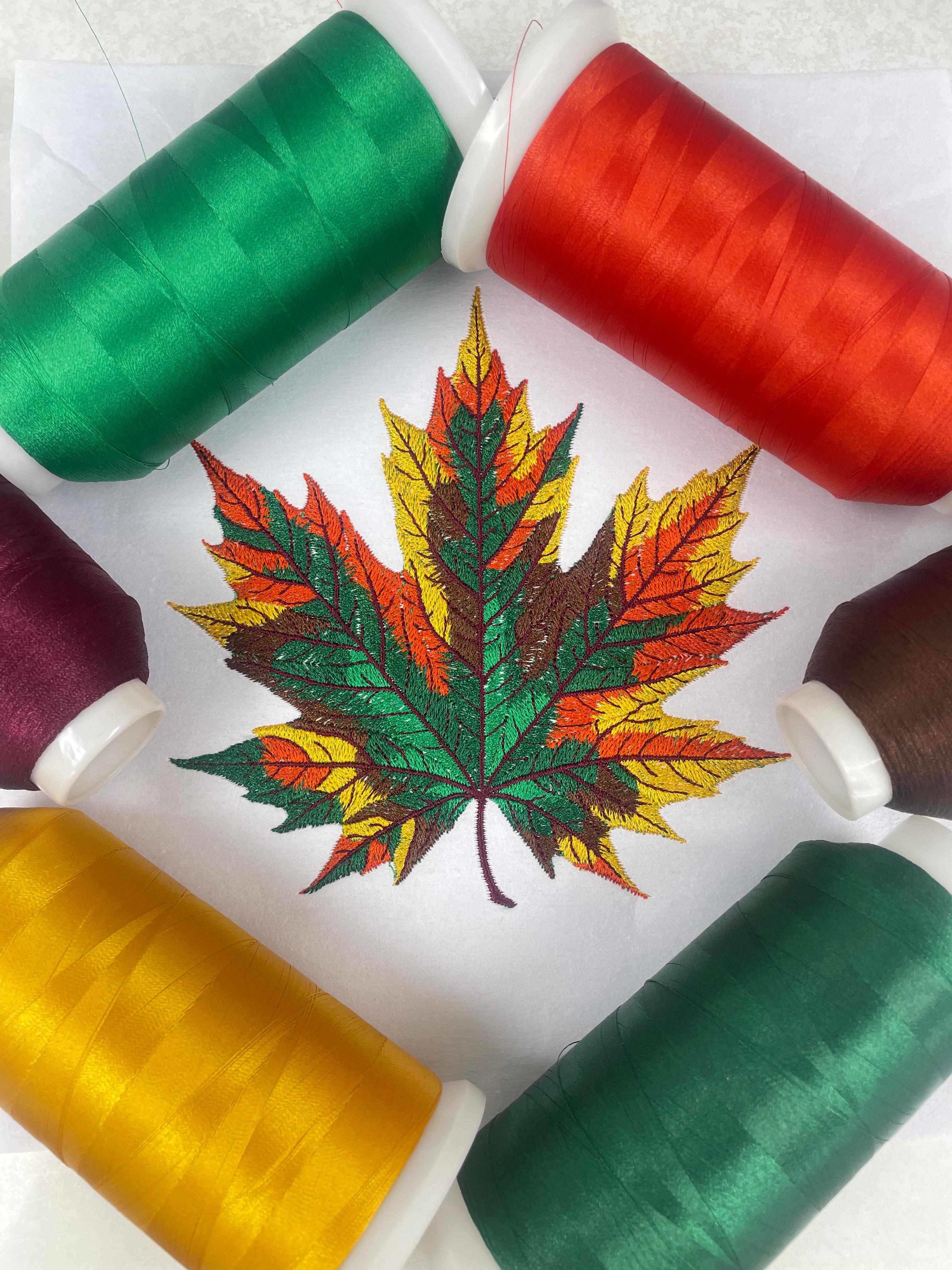 Spools of thread in green, red, purple, and yellow with a embroidered leaf design on a white background.