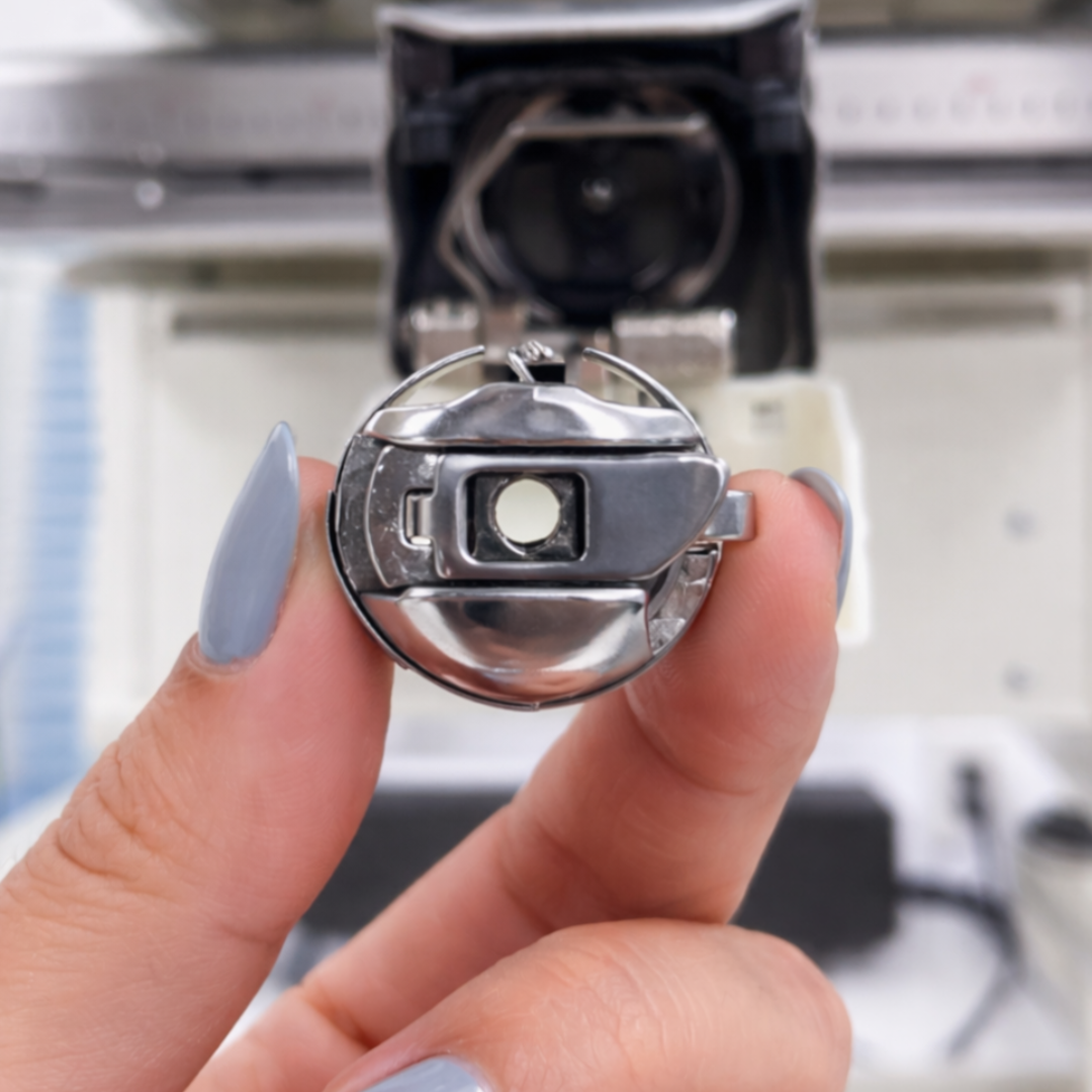 Close-up of a hand holding a pigtail bobbin case o a blurred background