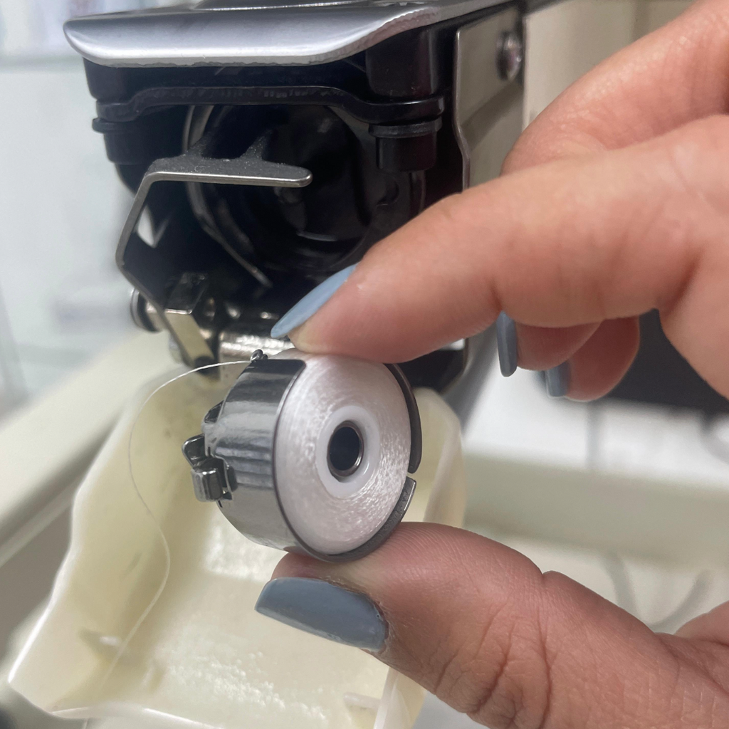 Person adjusting an embroidery machine's bobbin case.