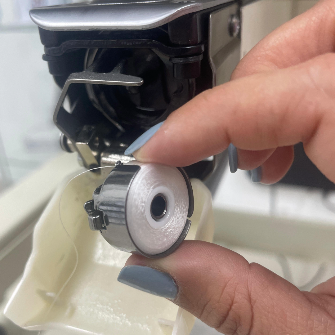 Person adjusting an embroidery machine's bobbin case.